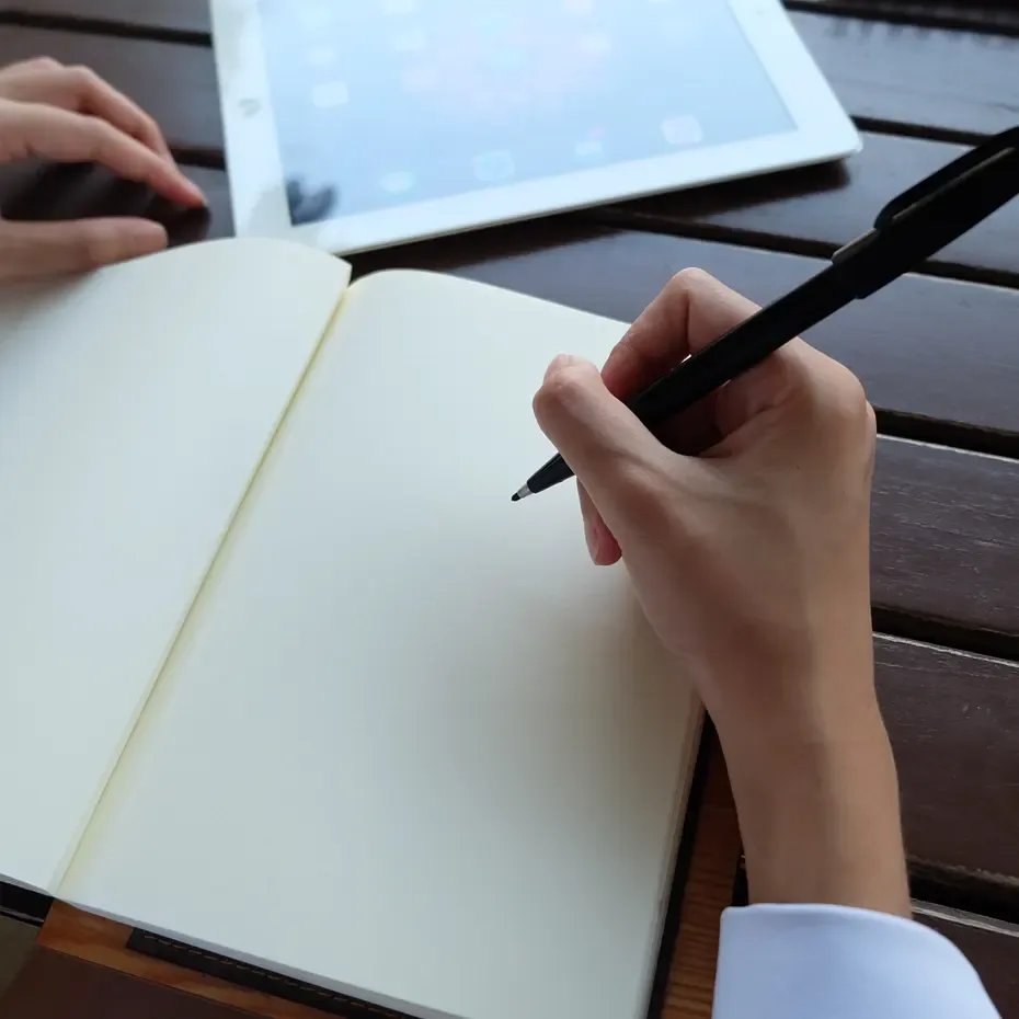 True Crime Akadémia, kézzel írt jegyzetek egy üres jegyzetfüzetben, mellette tablet, a bűnügyi cikk és prózaírás gyakorlati munkafolyamatának kezdete.